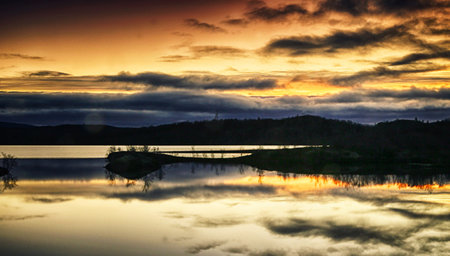 Sunset over a lake with reflection in the water and clouds in the skyの写真素材