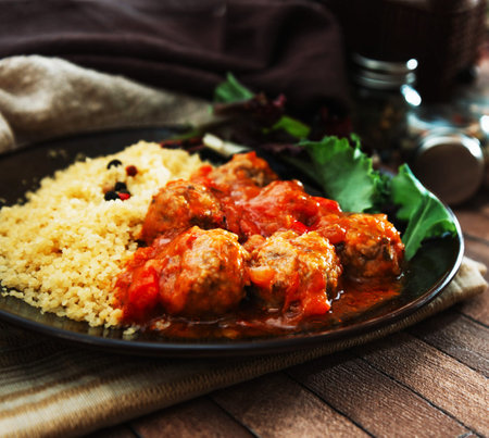 Meatballs in tomato sauce with couscous on a black plateの写真素材