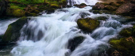 Long exposure of a waterfall flowing over rocks and mossy rocks.の写真素材