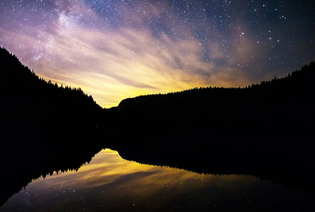 Milky way and stars over mountain lake at night with reflection in waterの写真素材