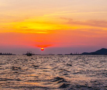 Sunset in the sea with fishing boats and mountains on the horizonの写真素材