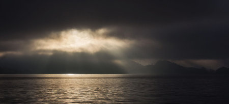 Sunset over the sea with clouds and mountains in the background.