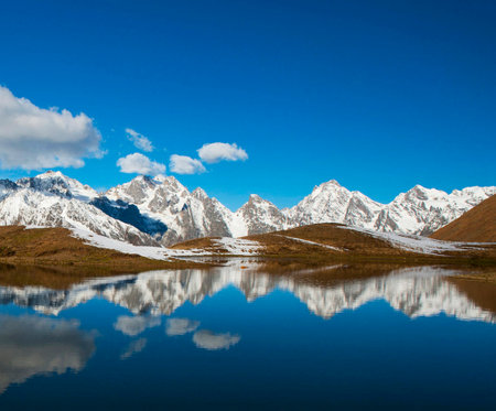 Mountain lake with reflection of snow-capped peaks and cloudsの写真素材