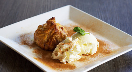 ice cream with baked apple on a white plate on a wooden table