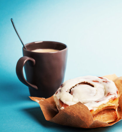 Cinnamon roll with cup of coffee on blue background. Shallow dof.の写真素材