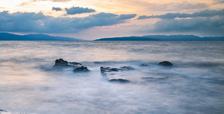Long exposure of a rocky beach with the sun setting behind the clouds