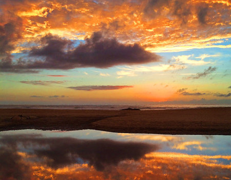 Sunset on the beach with reflection of clouds in the water.