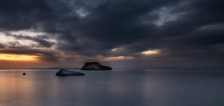 Sunset over the sea with rock in the foreground and dark sky