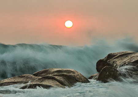 Sunset over the sea with rocks and waves in the foreground.の写真素材