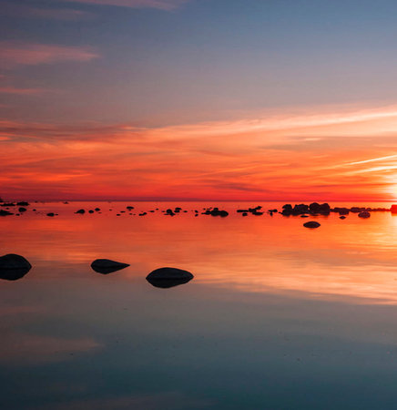 Sunset over the sea with stones in the foreground and reflection in the waterの写真素材