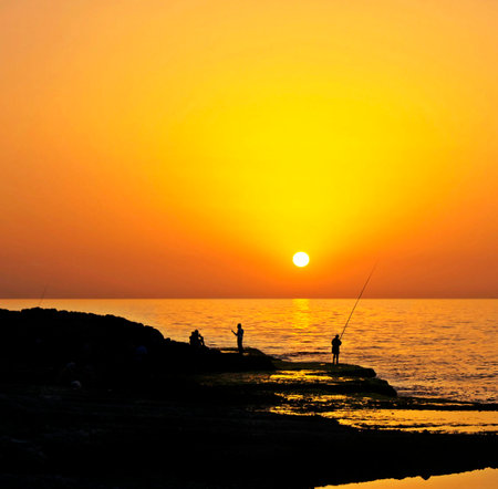 Silhouette of fishermen at sunset on the seashore.の写真素材