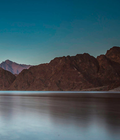 Landscape of mountains and lake with reflection in water at sunset.