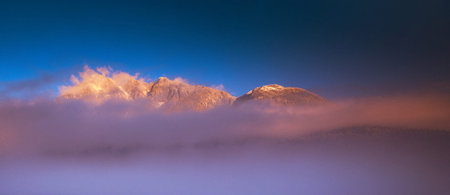 Panoramic view of the snow-capped mountains in the fog at dawn