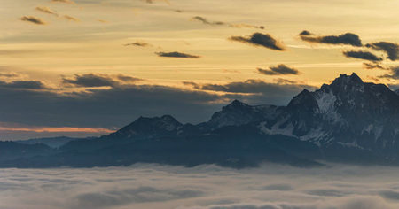 Panoramic view of a mountain range in the clouds at sunsetの写真素材