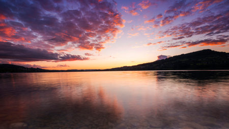 Sunset over the lake with clouds reflected on the water surface.