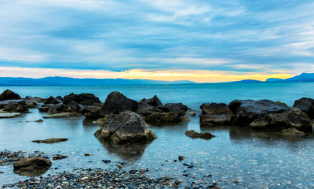 Sunset on the beach with rocks and pebbles in the foregroundの写真素材