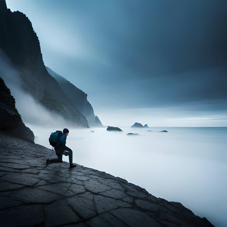 Man with backpack and trekking poles standing on the edge of a cliff at sunriseの素材