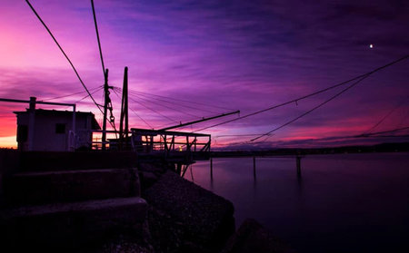 Sunset over the sea with fishing nets and a house in the foregroundの写真素材