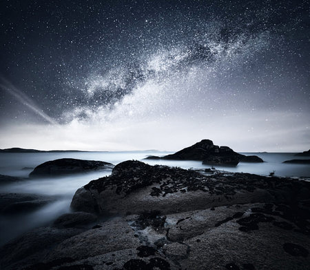 Milky way over the sea with rocks and starry sky.