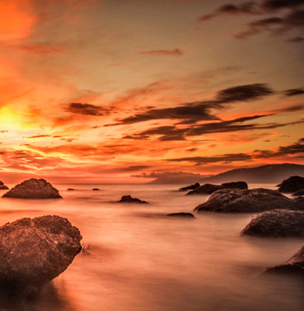 Sunset at the beach with rocks and sea in the foreground.の写真素材