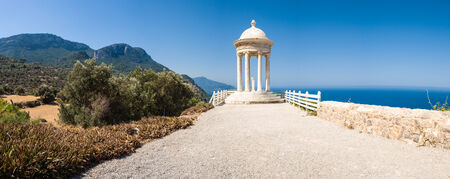 White marble medieval rotunda overlooking clear blue sea and sweeping mountains.の写真素材