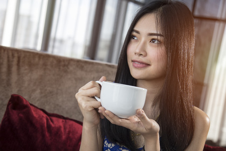 Beautiful Asian girl with cup of cofee mocha drinking in luxury home with sunlight in windows.  Copy space for text.の写真素材