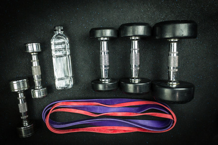 Fitness equipment for workout preparation and training with dumbbells and weights on the floor with bottle of water and bands.の写真素材