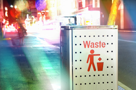 Trash bin on street sidewalk in the night with traffic and urban city lifestyle surrounding it.  World garbage and trash awareness.の写真素材