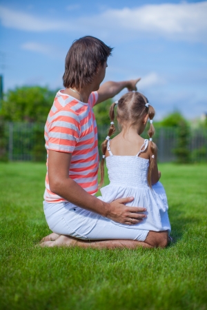Back view of father with his daughter sitting in the yard outdoorsの写真素材