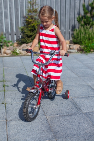 Little cute girl rides a bicycle in the dress in the yardの写真素材