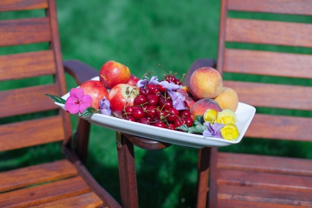 Plate with fresh fruits and flowers on wooden chairs in the gardenの写真素材