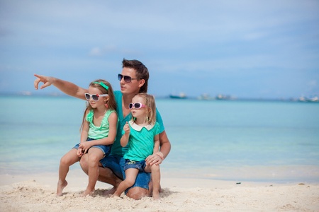 Happy father with his two daughters sitting on tropical beach vacationの写真素材