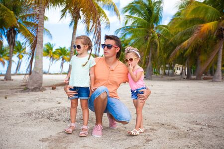 Young dad and his cute fashion daughters on tropical sand bech in palm groveの写真素材