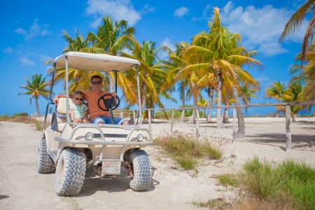 Dad and his two daughters driving golf cart at tropical countryの写真素材