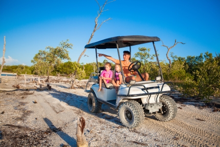 Dad and his two daughters driving golf cart at tropical beachの写真素材