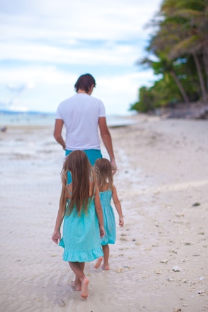 Back view of father and his two little daughters walking by the seaの写真素材