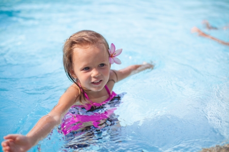 Little cute happy girl with flower behind her ear has fun in the swimming poolの写真素材