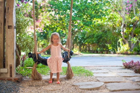beautiful little girl swinging on a swing in a cozy lovely flowered courtyardの写真素材
