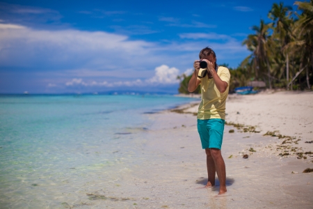 In front of the camera young man with camera in hand on beautiful white sandy beachの写真素材