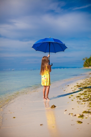 little girl with an umbrella in hands on her toes on the sandy white beachの写真素材