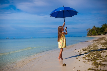 little girl with an umbrella in hands on her toes on the sandy white beachの写真素材
