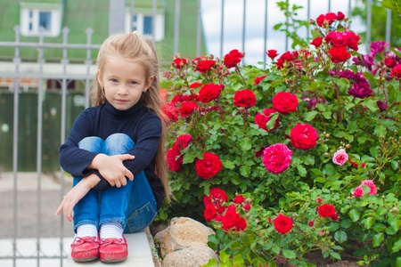 Portrait of cute little girl near the flowers in the yard of her houseの写真素材