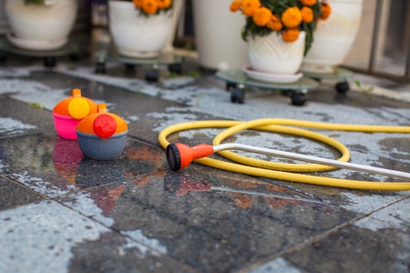 Children's bright watering can and a long hose on the wet ground in the yardの写真素材