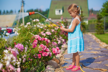 Ð¡ute girl in blue dress watering flowers with a hose in her gardenの写真素材