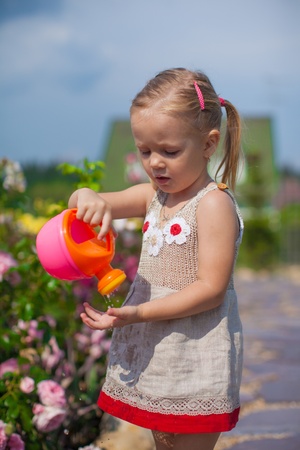 Adorable cute girl watering flowers with a watering canの写真素材