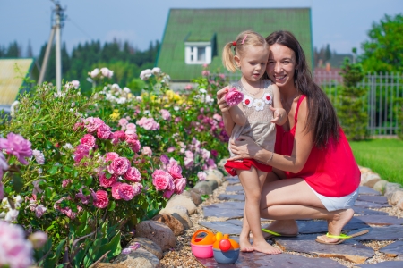 Young mother with her cute daughter near flowers in the gardenの写真素材