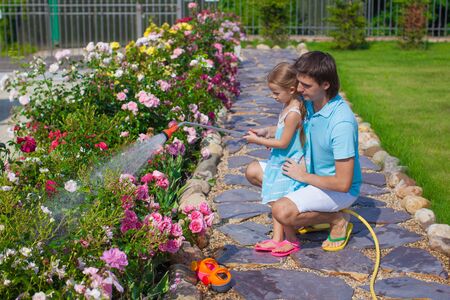 Little cute girl and father watering flowers with a hose in her gardenの写真素材
