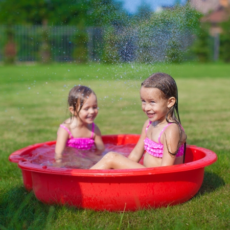 Two little sisters frolicing and splashing in their yard in small poolの写真素材