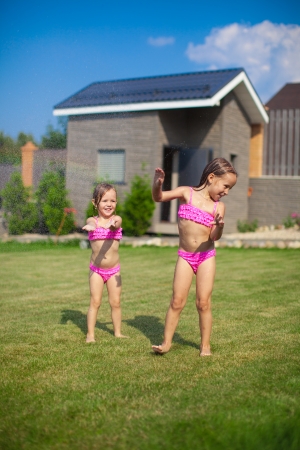 Two little sisters frolicing and splashing in their yardの写真素材