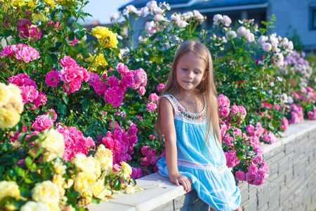 Little adorable girl sitting near colorful flowers in the gardenの写真素材